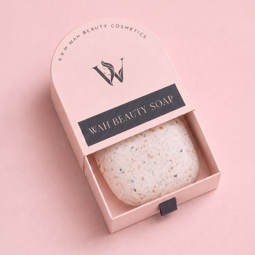 A pink arched cosmetic gift box with the lid partially open, revealing a speckled bar soap inside. The box lid is printed with the brand name 'R.R.M Wah Beauty Cosmetics' and a large 'W' logo, with a black label reading 'WAH BEAUTY SOAP'.