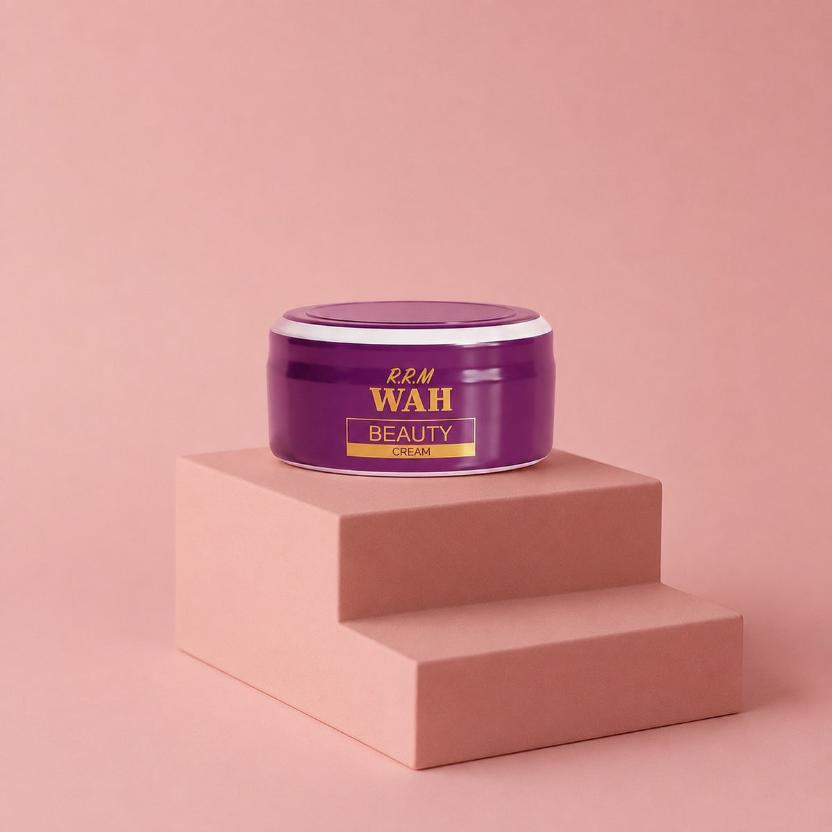 A purple cosmetic cream jar with gold lettering reading 'R.R.M WAH BEAUTY CREAM' sits on a two-tiered dusty pink pedestal against a matching pink background.